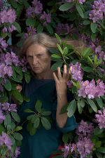 Künstlerin Lena Ursprung tritt aus einer Wand mit lila Blumen. 