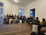 Gruppe von Menschen sitzt in einem hellen Raum bei einer Veranstaltung. 