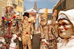 Bunte Faschingsmasken und -kostüme in einer traditionellen Aufstellung, mit Stadtkulisse im Hintergrund.